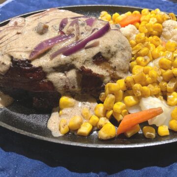 bacon wrapped filet mignon with mushroom sauce and a side of corn carrots and cauliflower