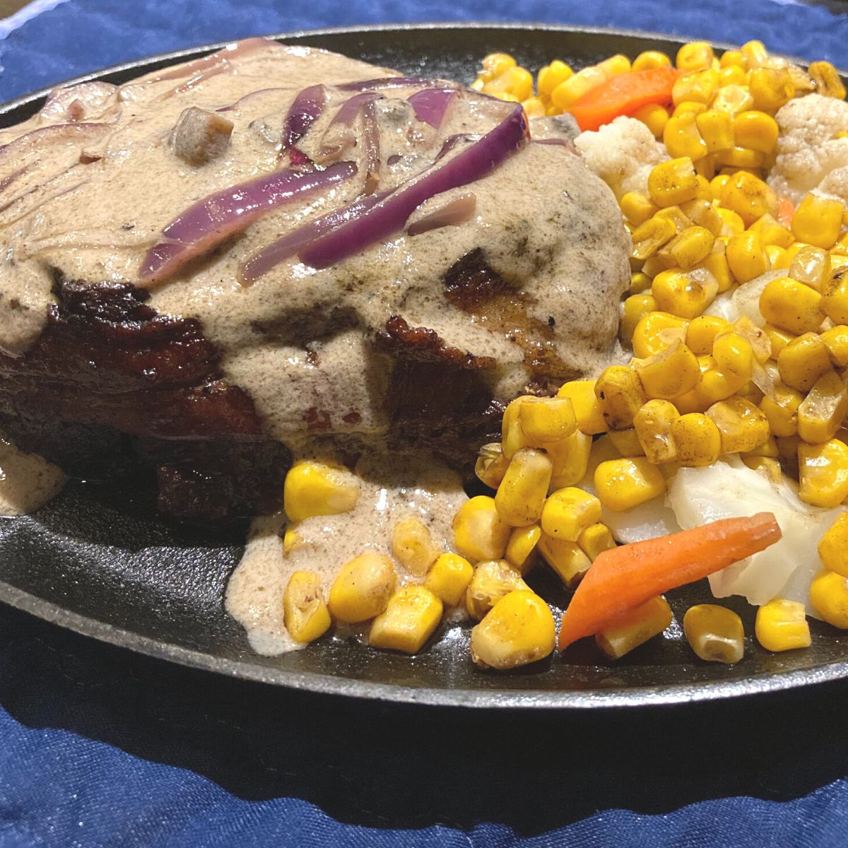 bacon wrapped filet mignon with mushroom sauce and a side of corn carrots and cauliflower